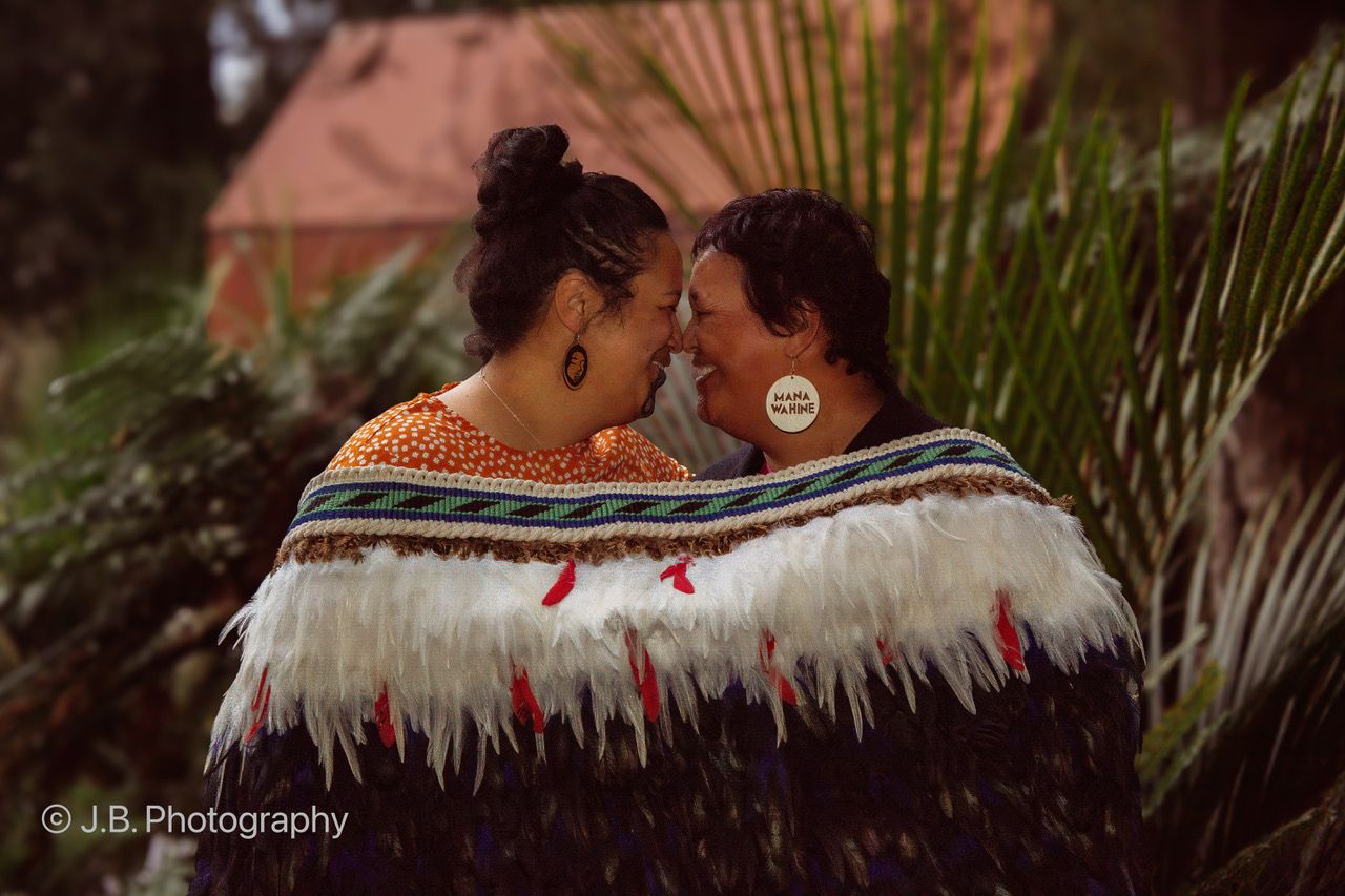 Two women in traditional Maori cloaks share an intimate hongi greeting outdoors.