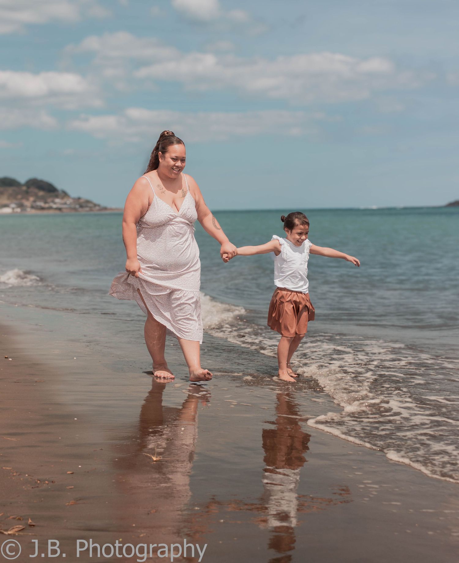 Mother and daughter run hand in hand along a sunny beach shoreline.