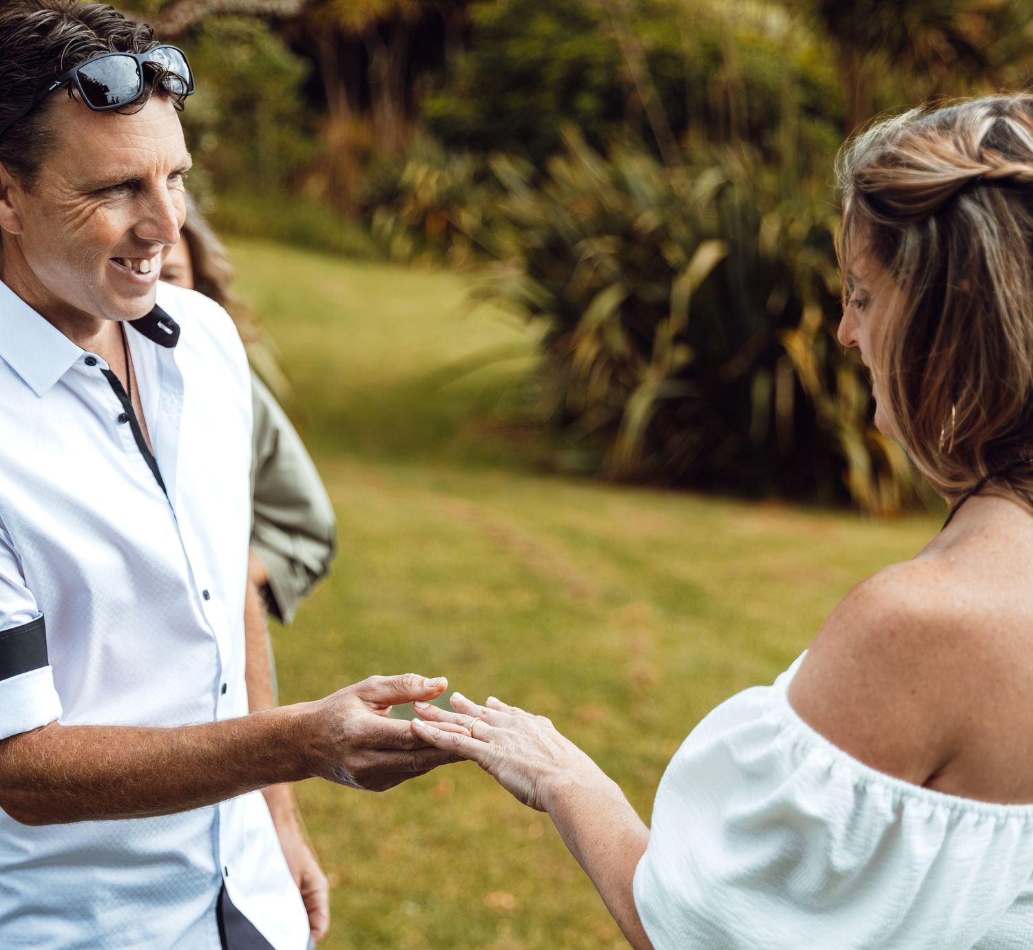 Smiling groom places wedding ring on brides hand during outdoor garden ceremony.