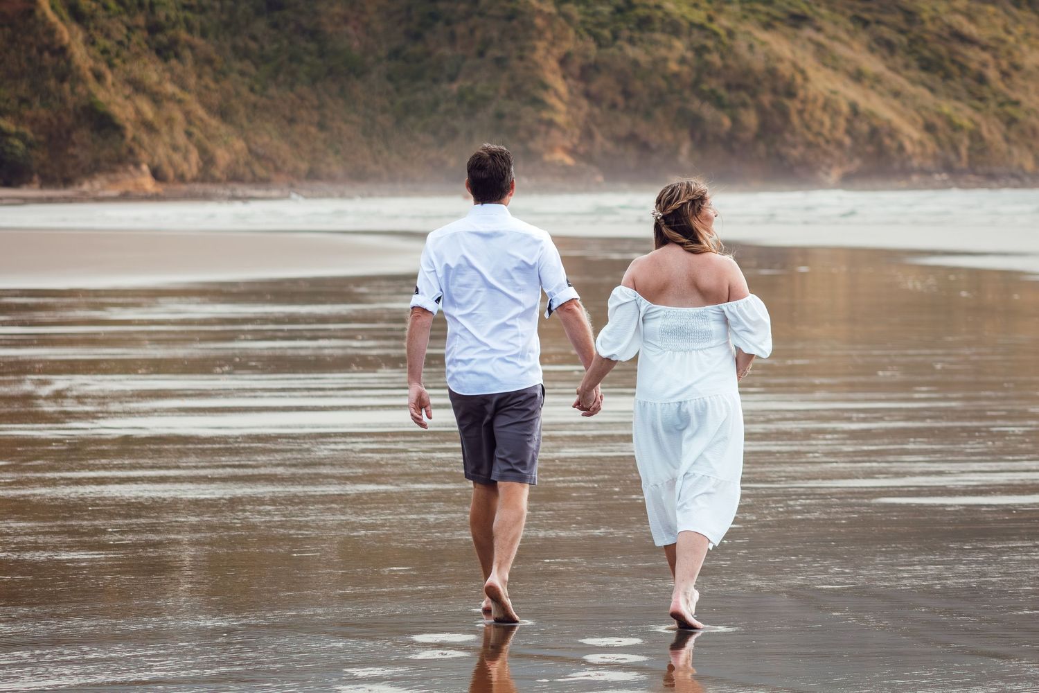 Newlywed couple walks hand in hand along a scenic misty beach after wedding.