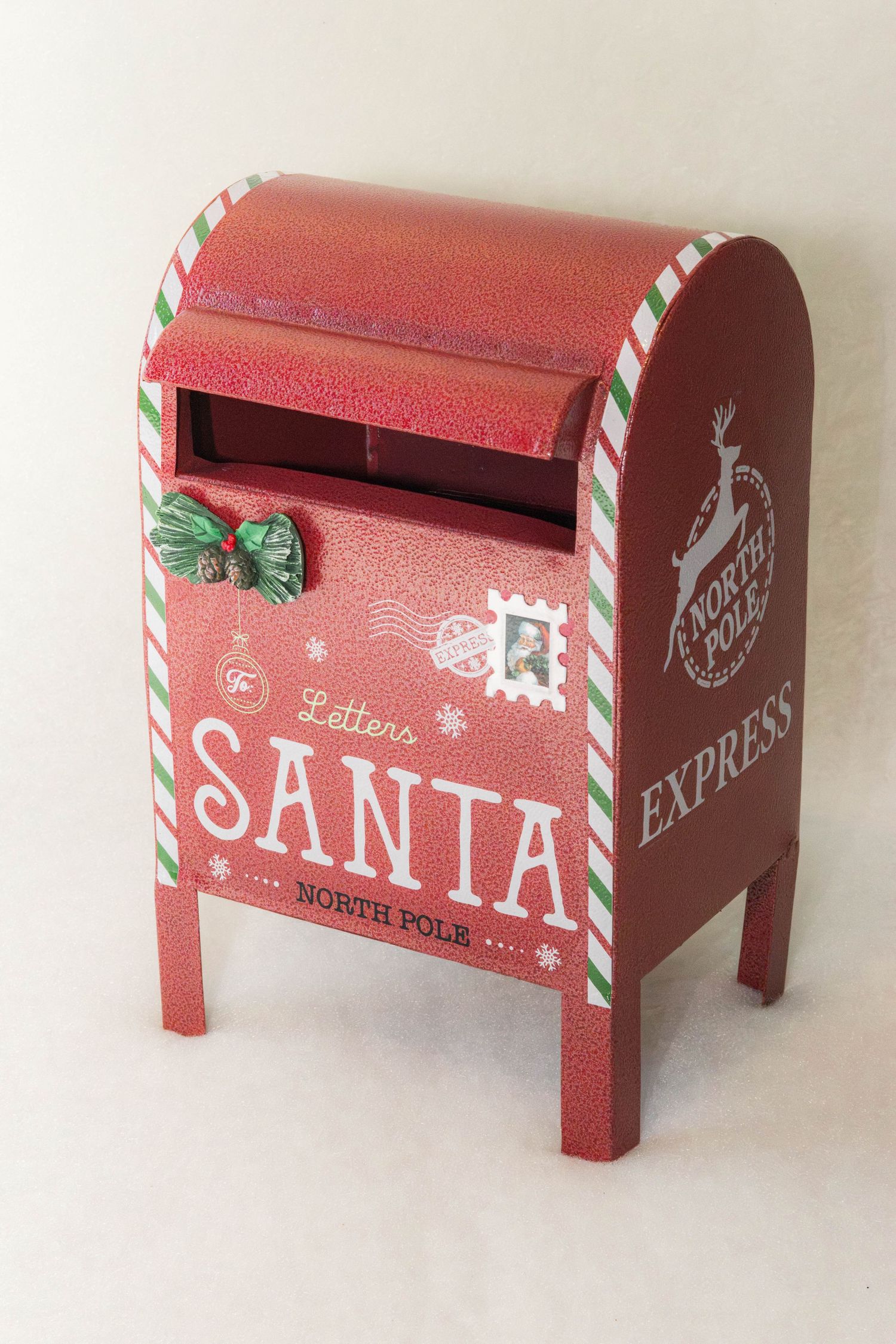 Red metal Santa letters mailbox with North Pole Express reindeer logo, candy cane striped edges, holly bow and vintage stamp design.