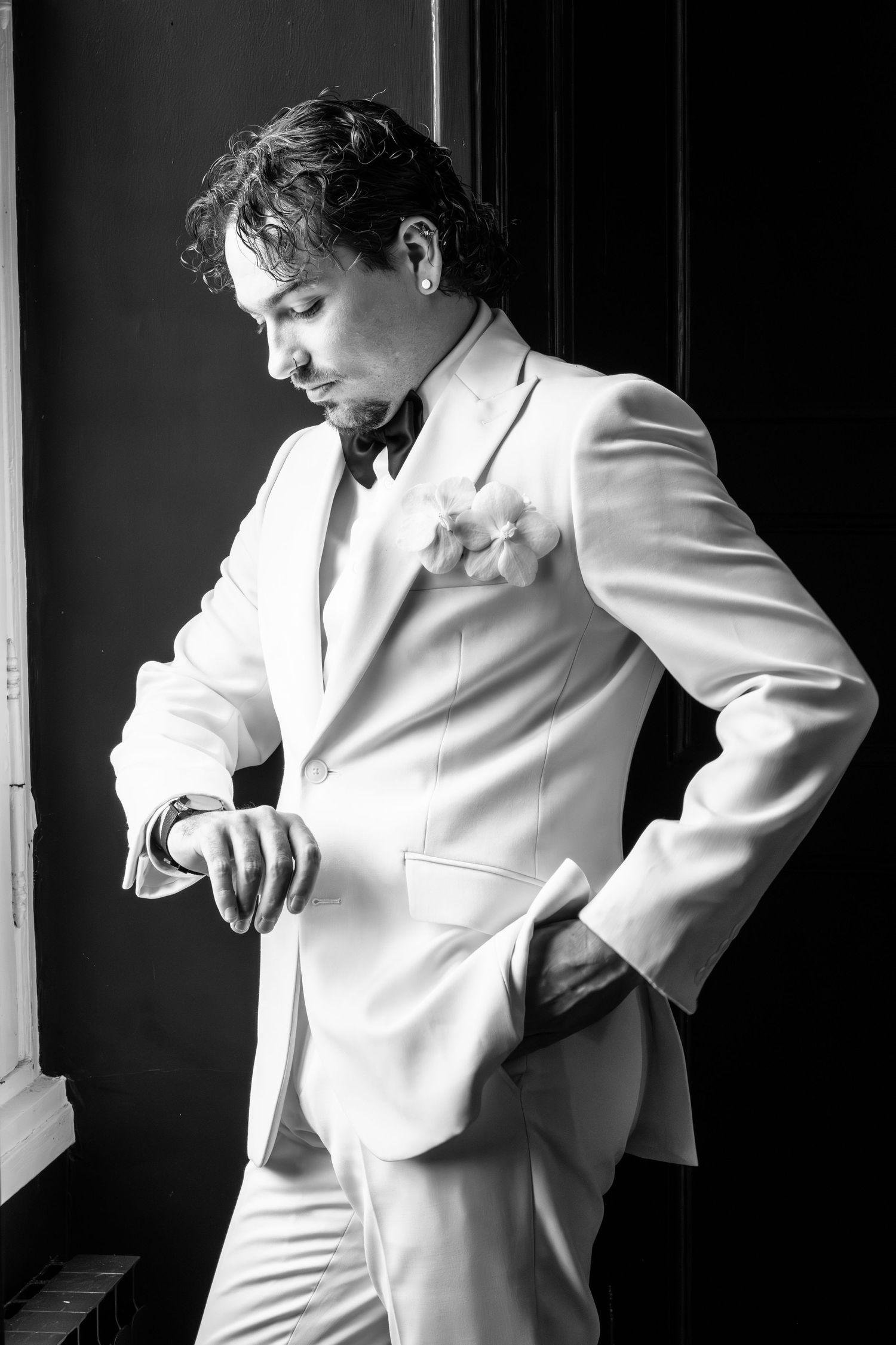 Black and white photo of a groom in white tuxedo checking his watch before wedding ceremony.