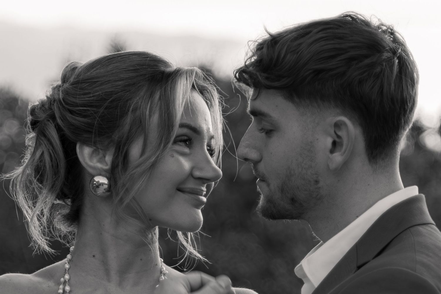 Black and white wedding photo of a smiling bride and groom gazing at each other outdoors.