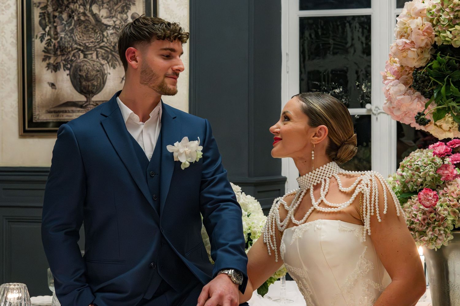 Bride and groom in elegant wedding attire smile at each other during their reception ceremony.