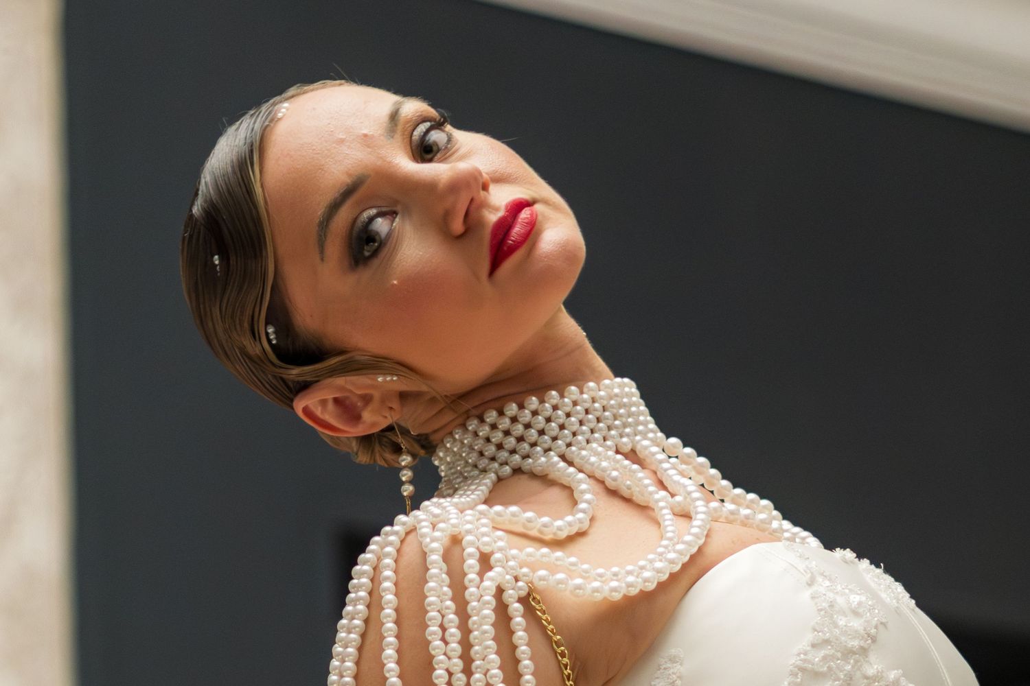 Elegant woman wearing layered pearl necklace and white dress, posing with red lips and sleek hair.