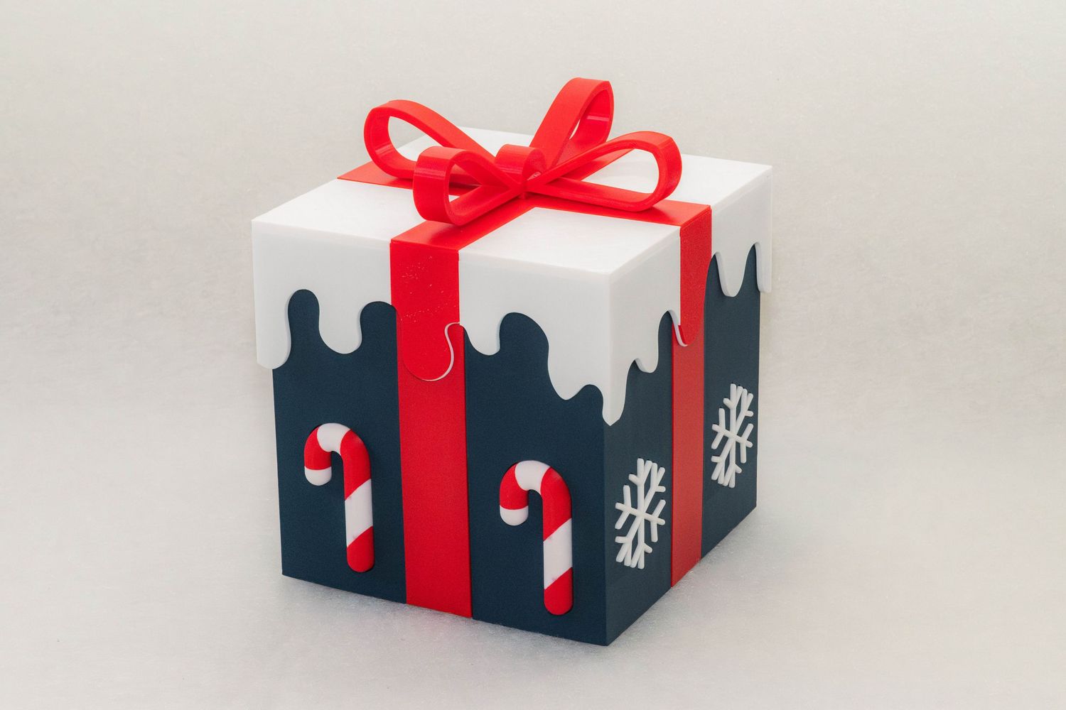 Christmas gift box with white snowy top, navy sides decorated with candy canes and snowflakes, tied with a red ribbon and bow.