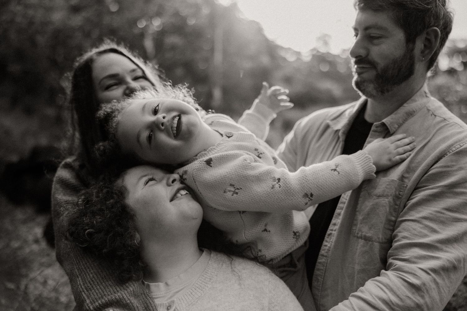 Black and white photo of a joyful family with two parents laughing as they hold their happy child outdoors in Newport Melbourne.