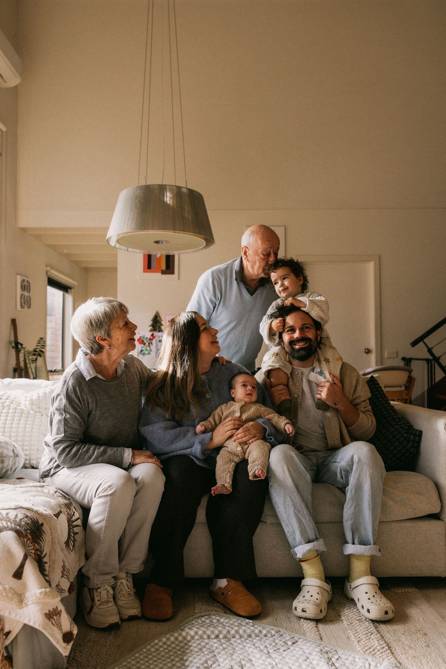 Multi-generational family portrait with grandparents, parents, and young children sitting together on a couch indoors in Melbourne.