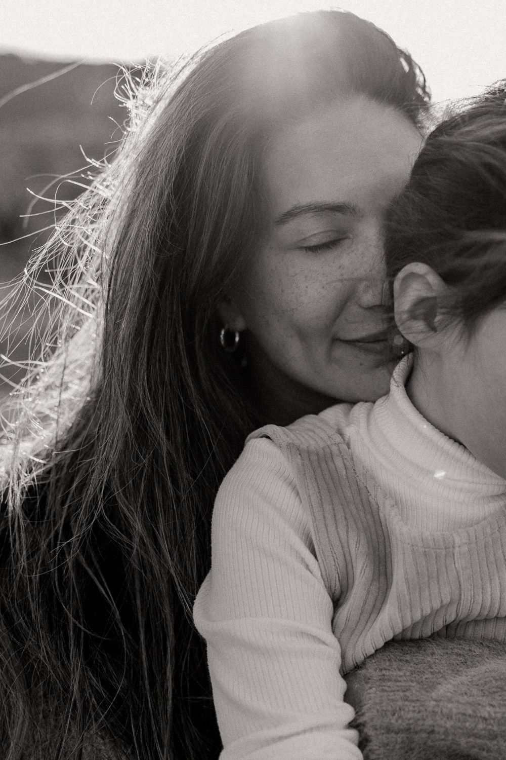 Black and white photo of a woman with freckles and long hair hugging her daughter in warm sunlight at You Yangs Regional Park Victoria.