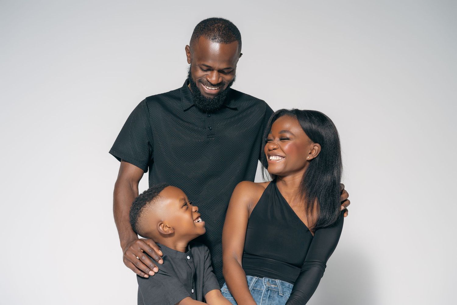 Happy Black family with father, mother, and young son laughing together in black outfits.