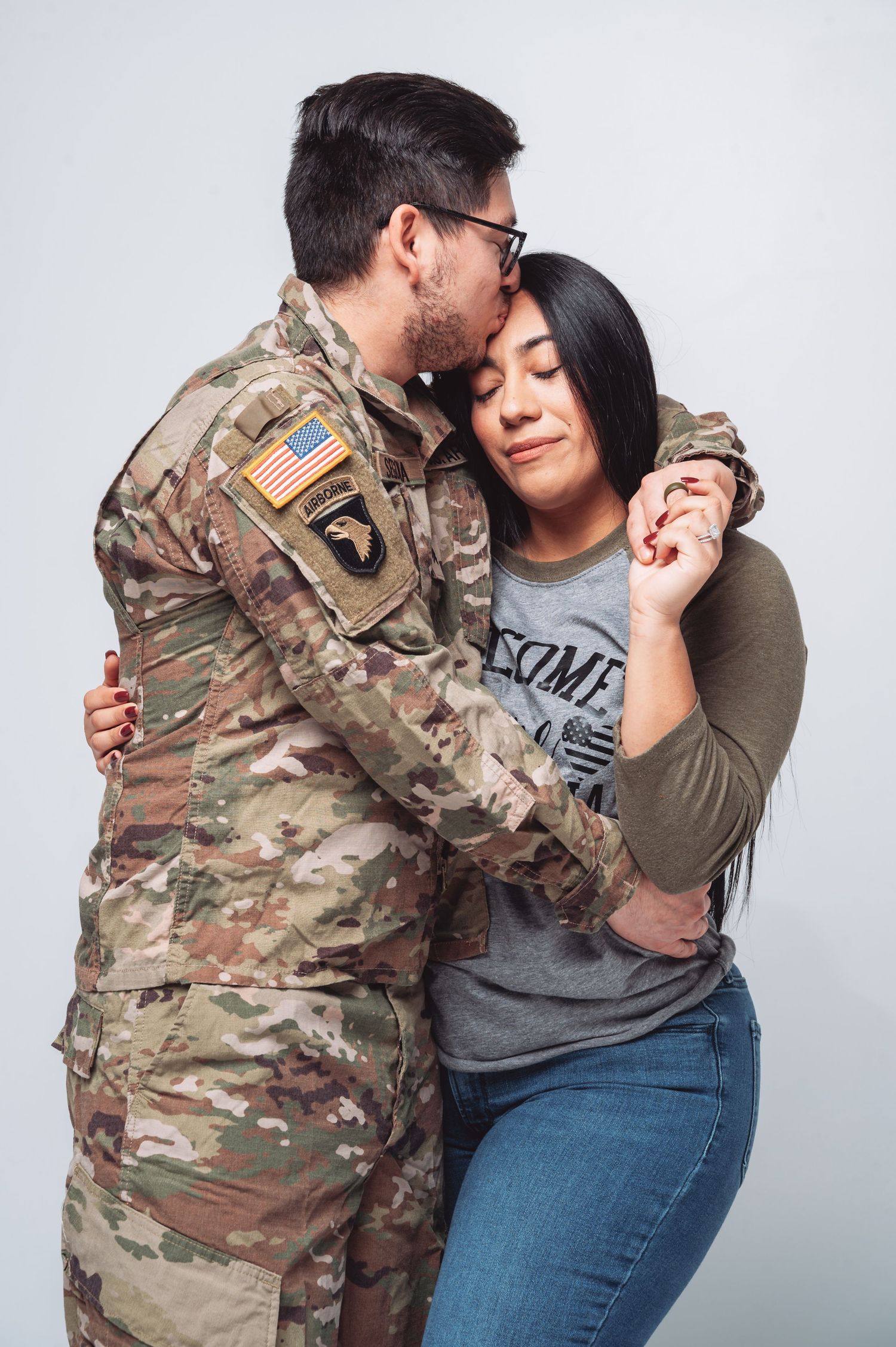 US Army soldier in camouflage uniform kissing his partner on the cheek in a tender embrace.