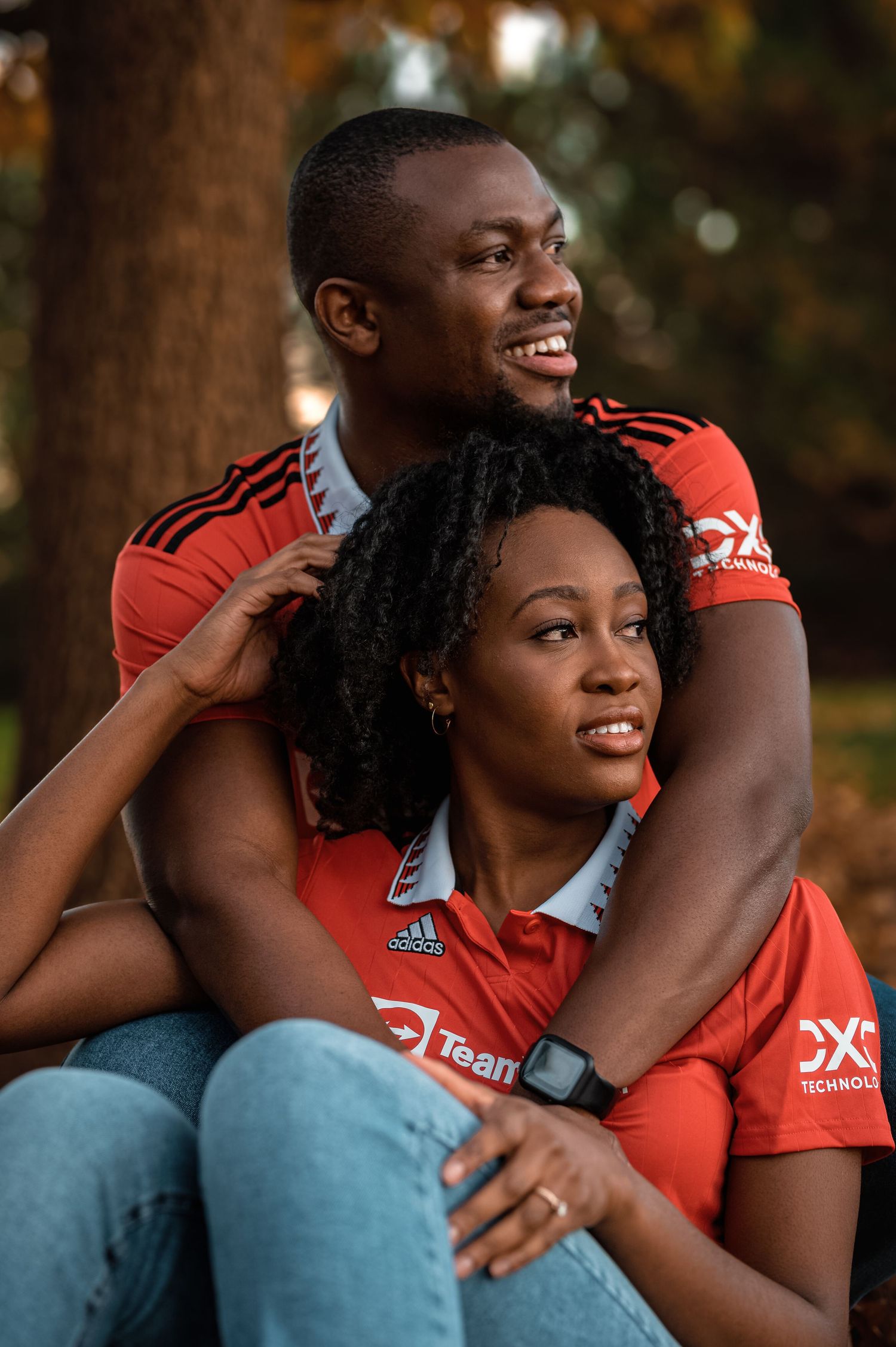 Happy Black couple in matching red Adidas jerseys embracing outdoors near trees.