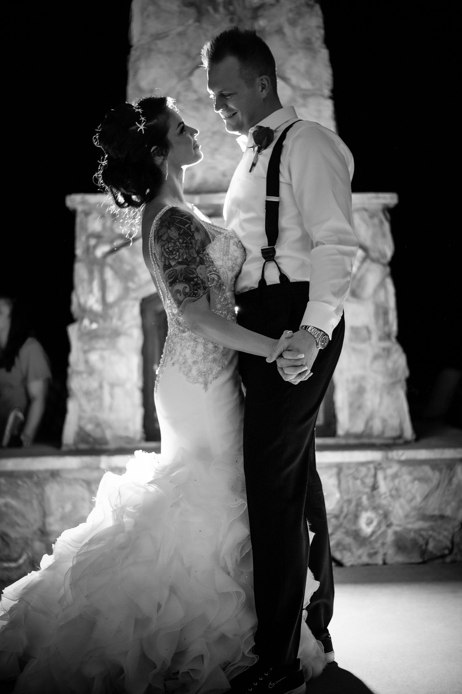 Black and white photo of bride and groom sharing first dance near stone fireplace.