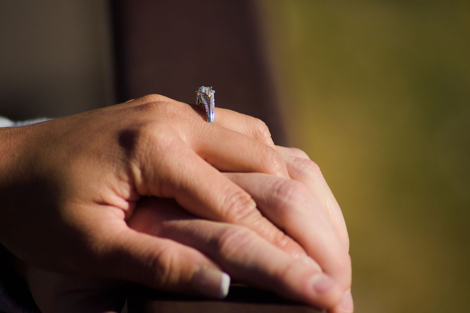 Close-up of folded hands displaying a diamond solitaire engagement ring in soft light.