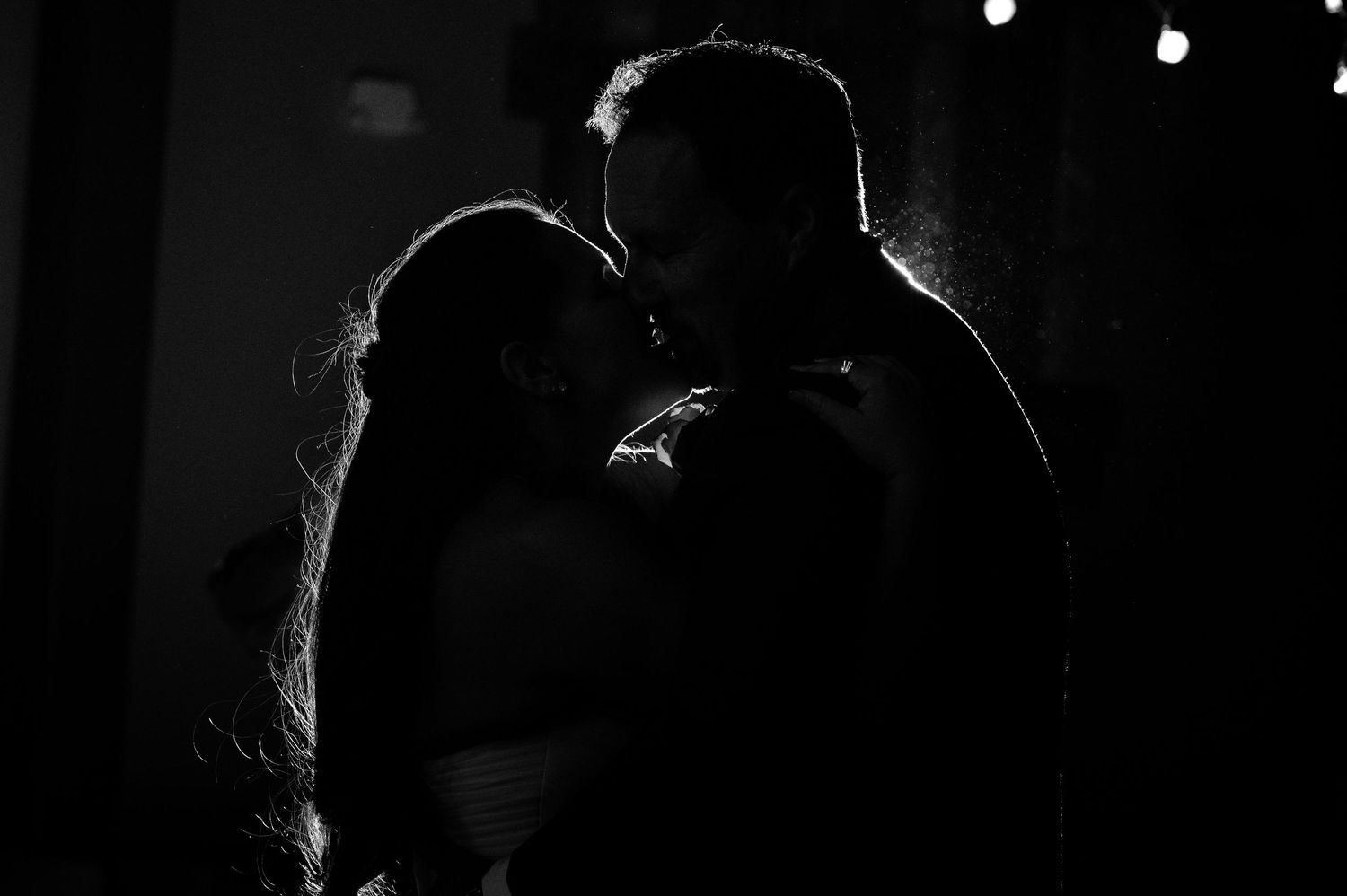 Romantic black and white silhouette of bride and groom sharing a kiss at wedding reception.