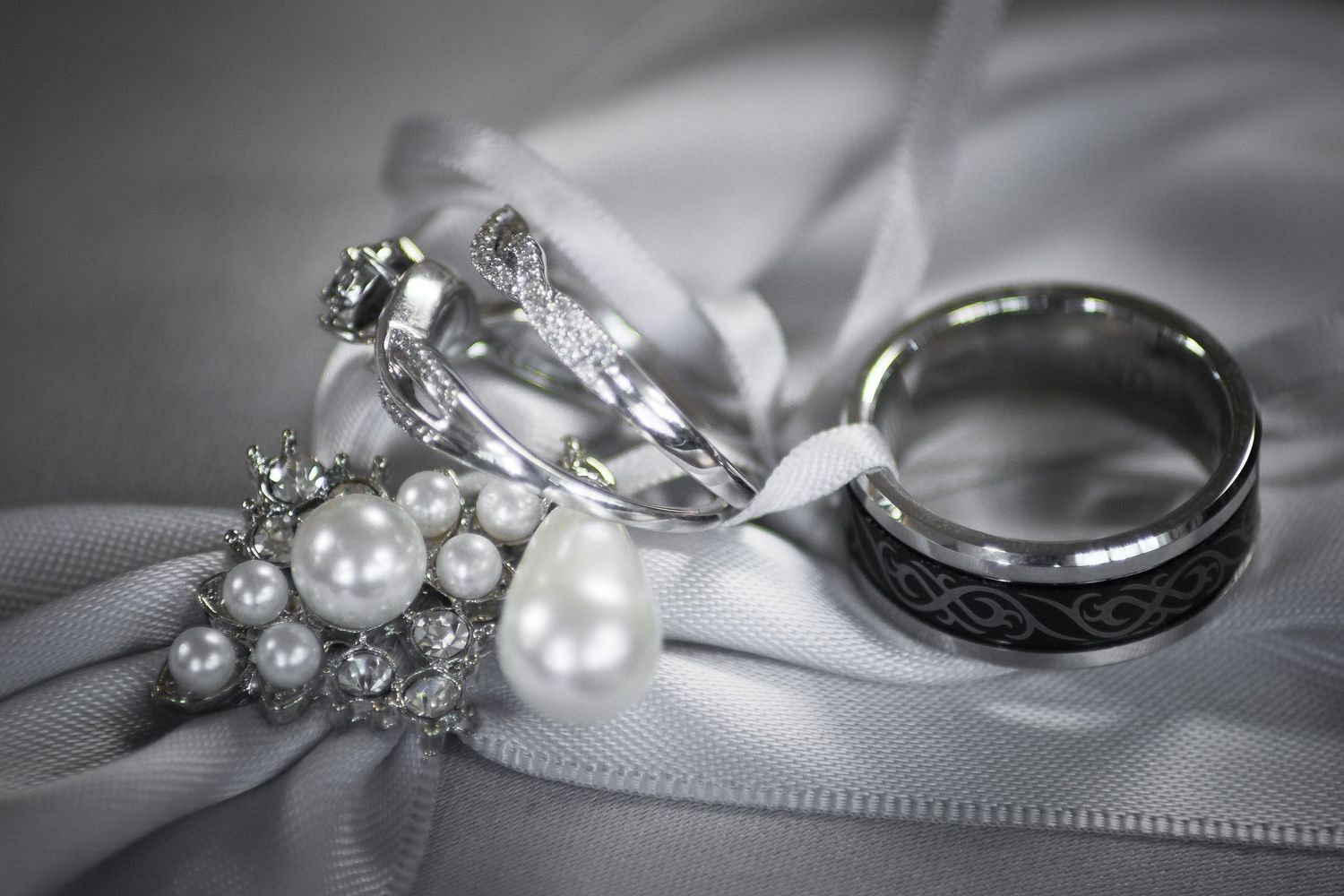 Close-up of elegant wedding rings and pearl bracelet arranged on white satin ribbon.