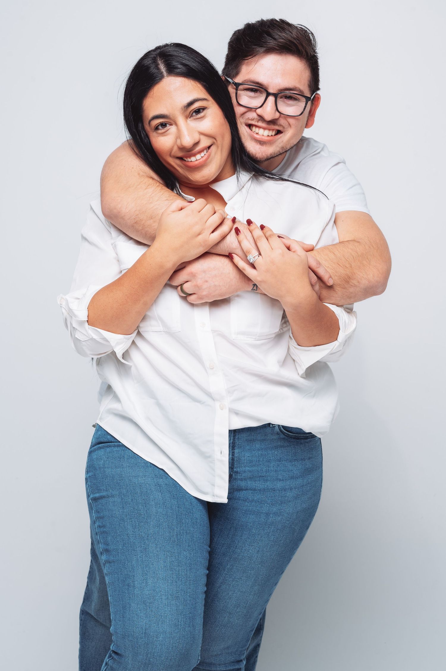 Happy couple hugging and smiling against white background, man with glasses embracing woman in white shirt and jeans.