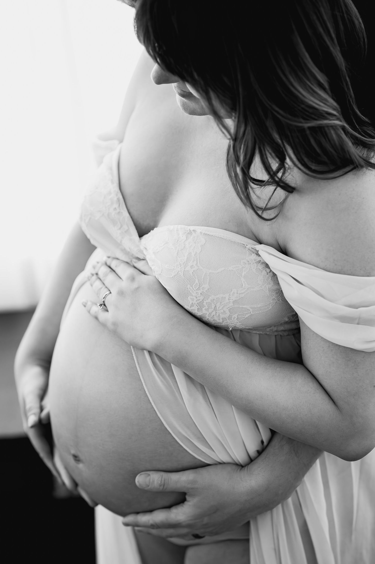 A black and white close-up of a pregnant woman in lace lingerie cradling her bare baby bump.