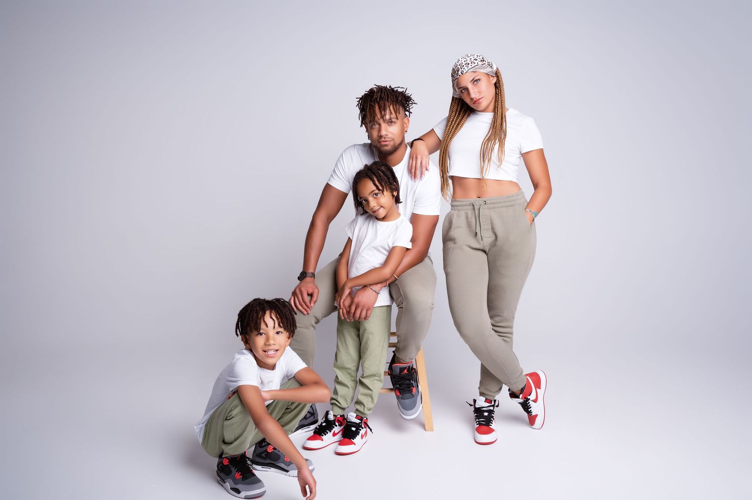 Stylish family of four in matching white and olive outfits posing together in a photo studio.