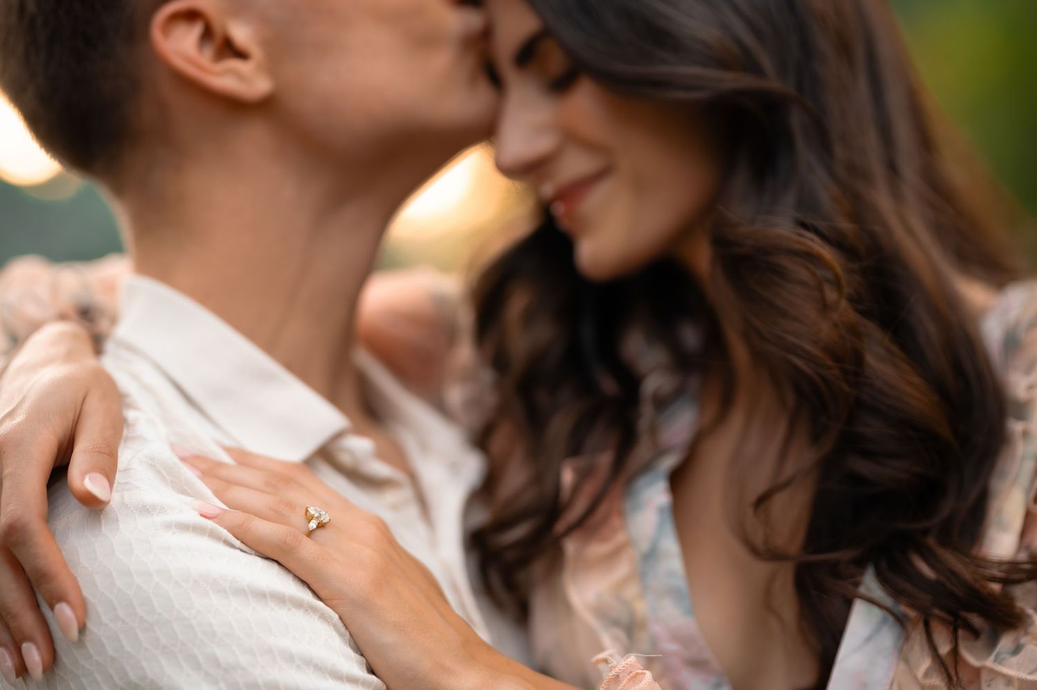 Romantic couple sharing an intimate moment, woman wearing a gold engagement ring, soft bokeh background.