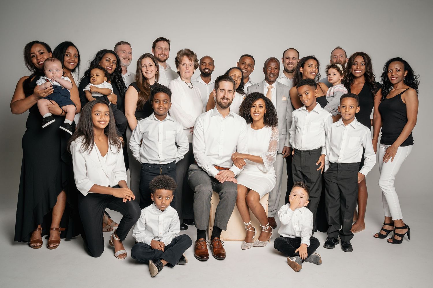 Large multigenerational family portrait with adults and children in white and black attire.