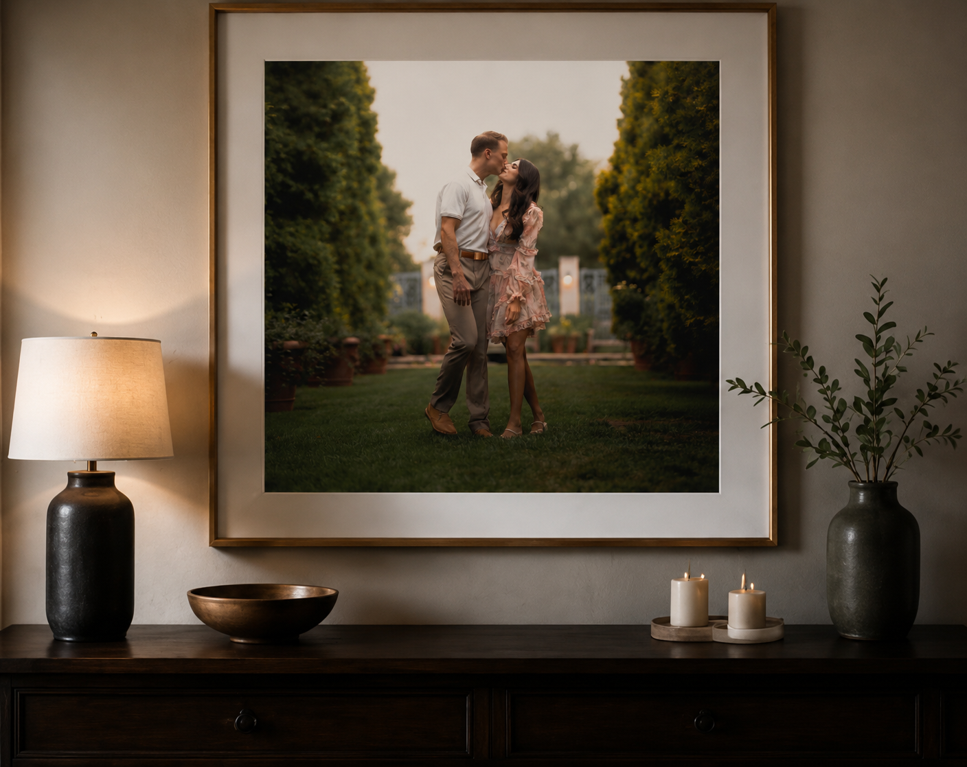 Framed fine art print of couple embracing in lush garden displayed above wooden console table.