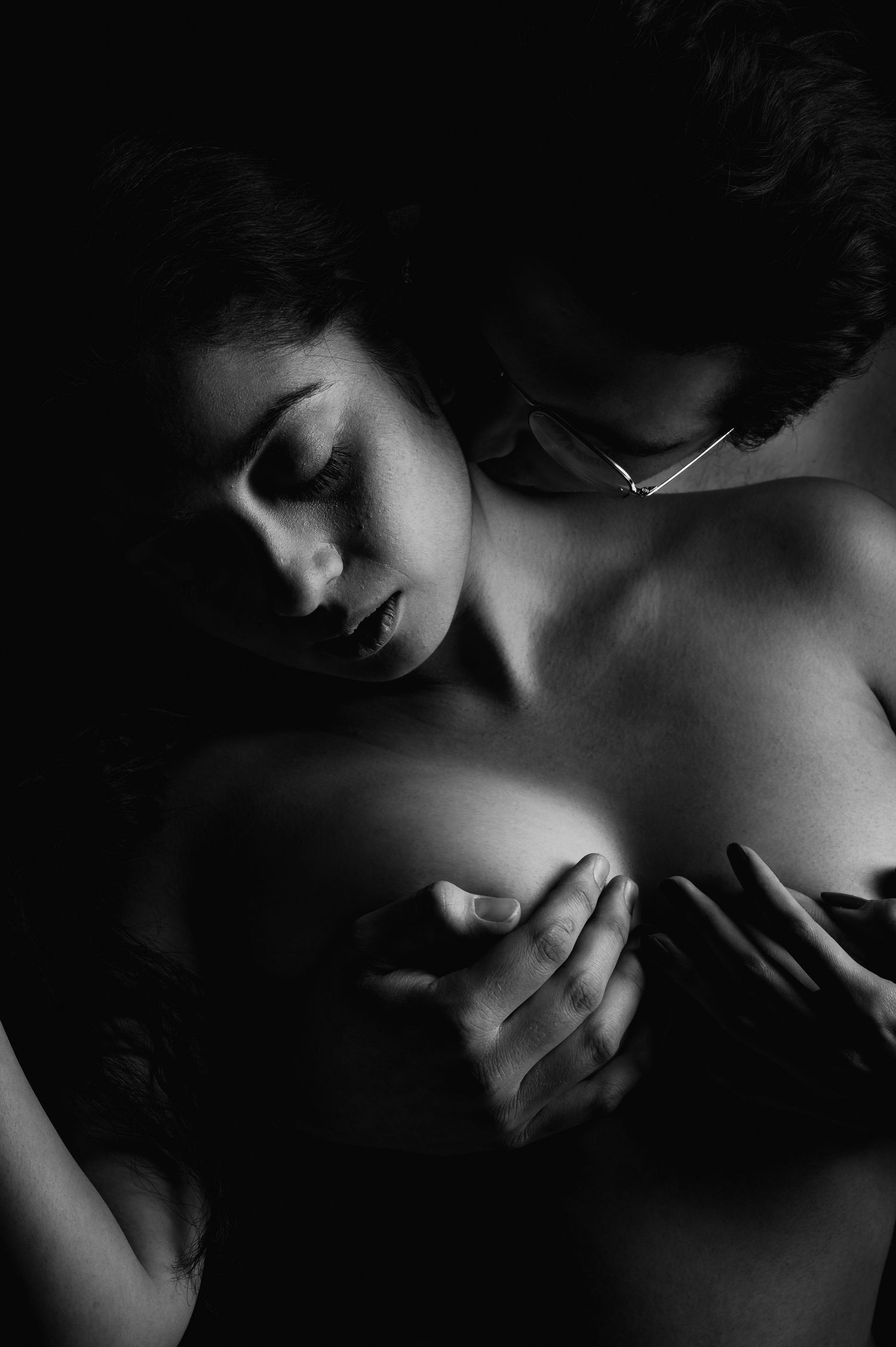 Black and white intimate couple photography with dramatic chiaroscuro lighting highlighting sensual embrace.