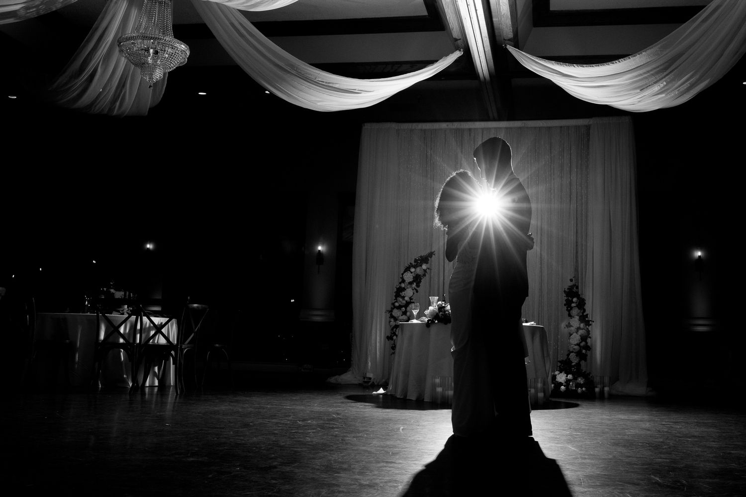 Dramatic black and white silhouette of bride standing alone in ballroom spotlight.