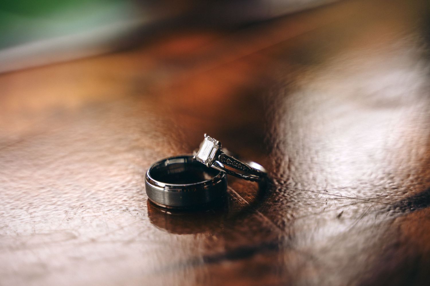 Two wedding rings, one black band and one diamond engagement ring, on wooden surface.