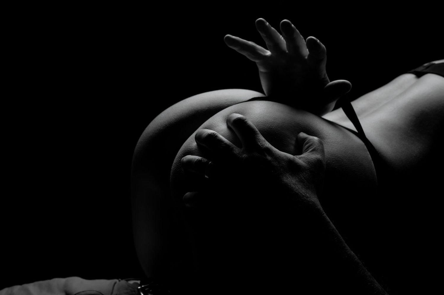 Black and white artistic silhouette of woman in lingerie cradling husband against dark background.