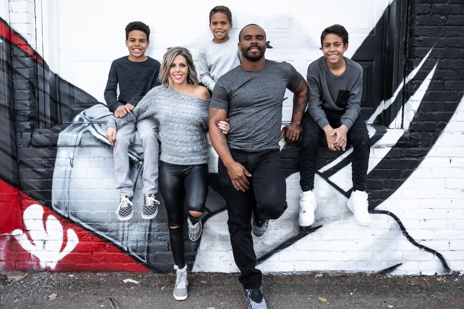 Interracial family of five posing casually in front of a colorful street mural outdoors.