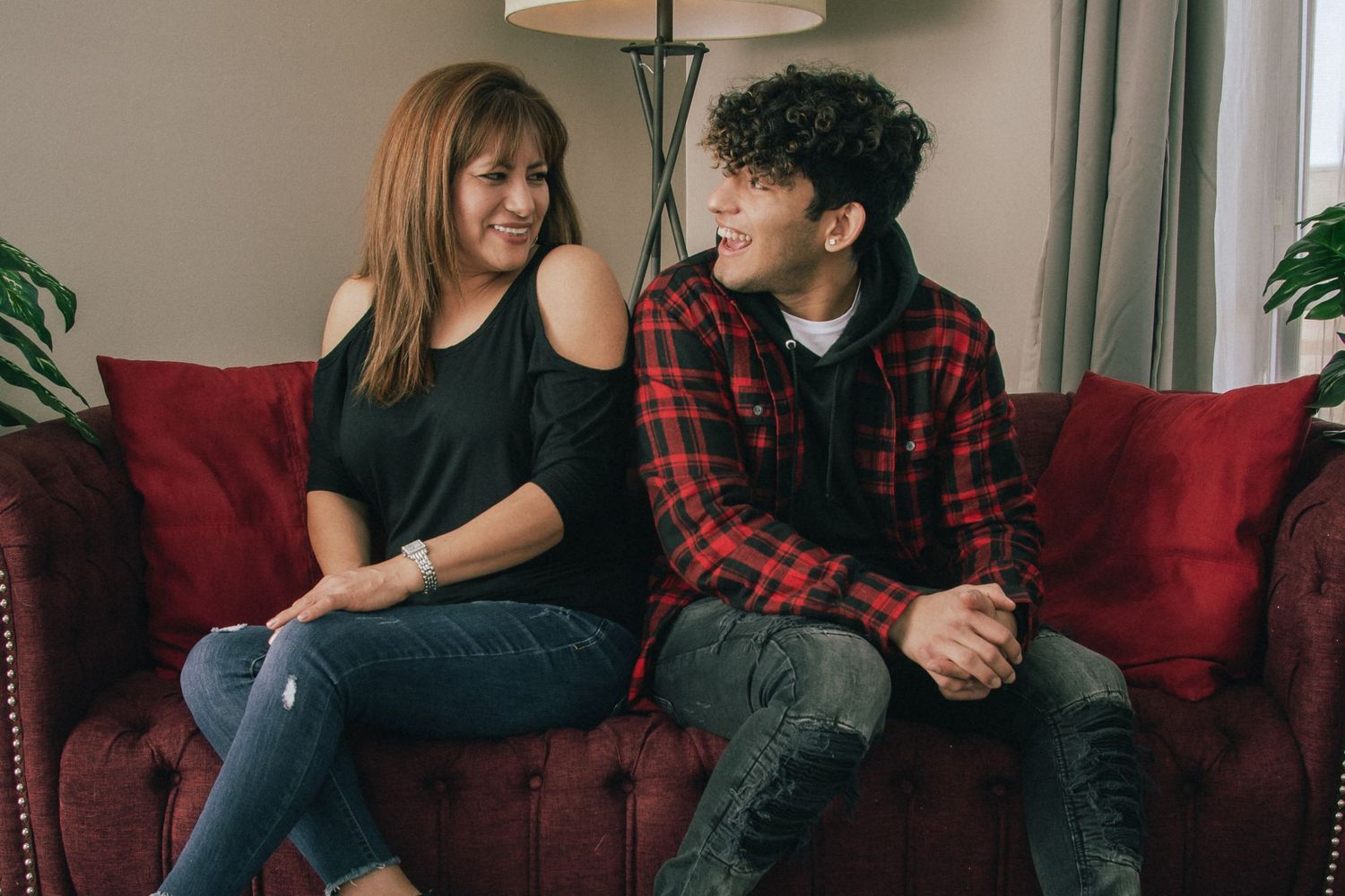 Mother and teenage son sharing a laugh while sitting together on red velvet sofa.