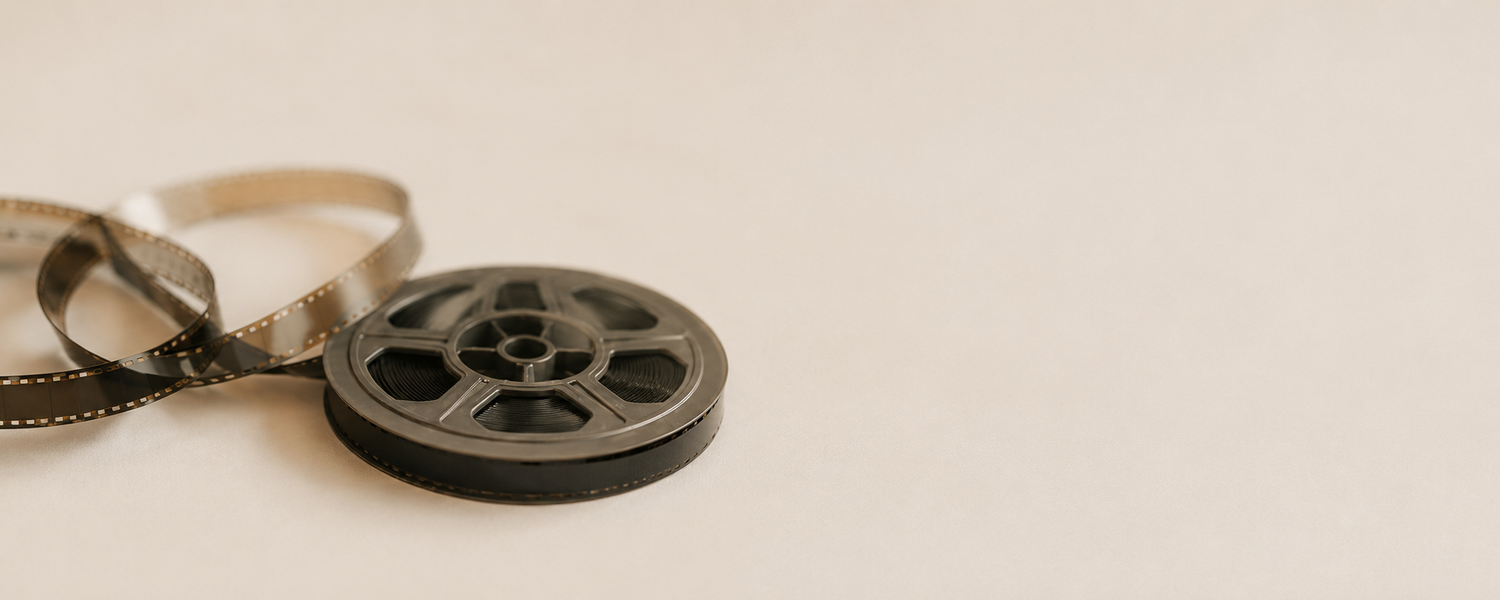 A classic 35mm film reel with loose filmstrip on a neutral beige background for vintage cinema themes.