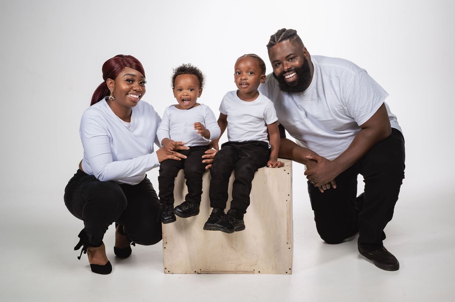 A Black family of four with two young children posing together in a white studio setting.