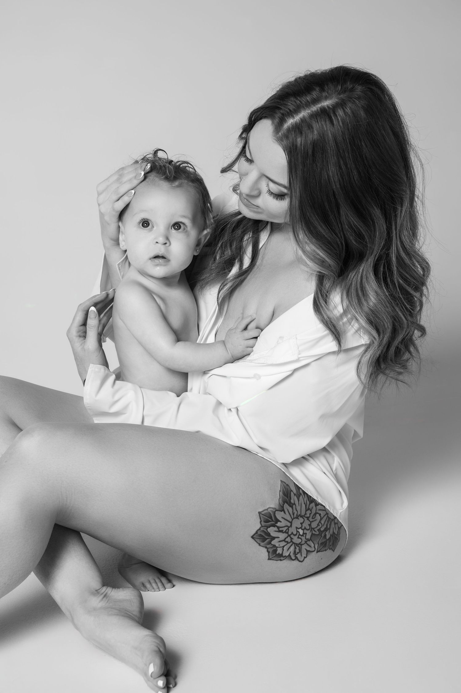 Black and white studio photo of a young mother holding her curious baby infant.
