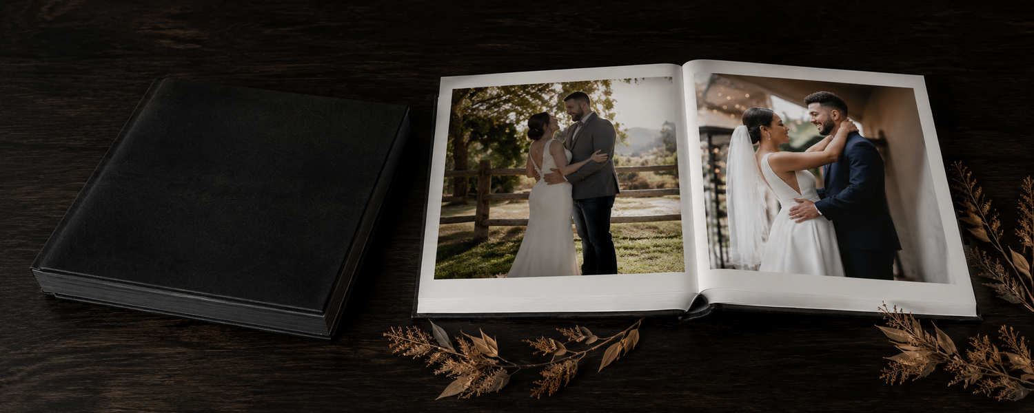 Open wedding photo album displaying romantic couple portraits on a dark wooden surface with decorative wheat stems.