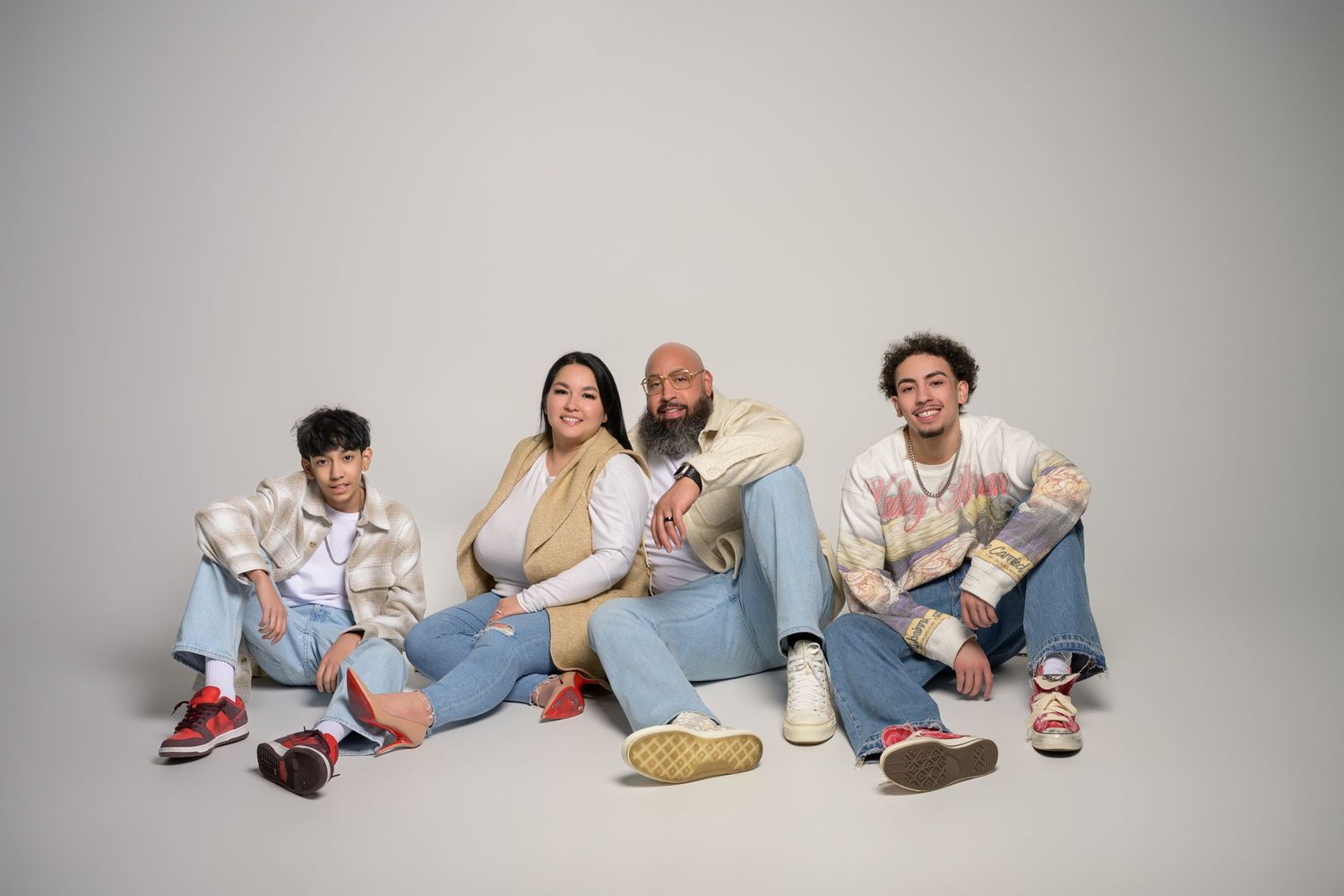 Hispanic family of four sitting casually on floor in coordinated denim outfits in studio.