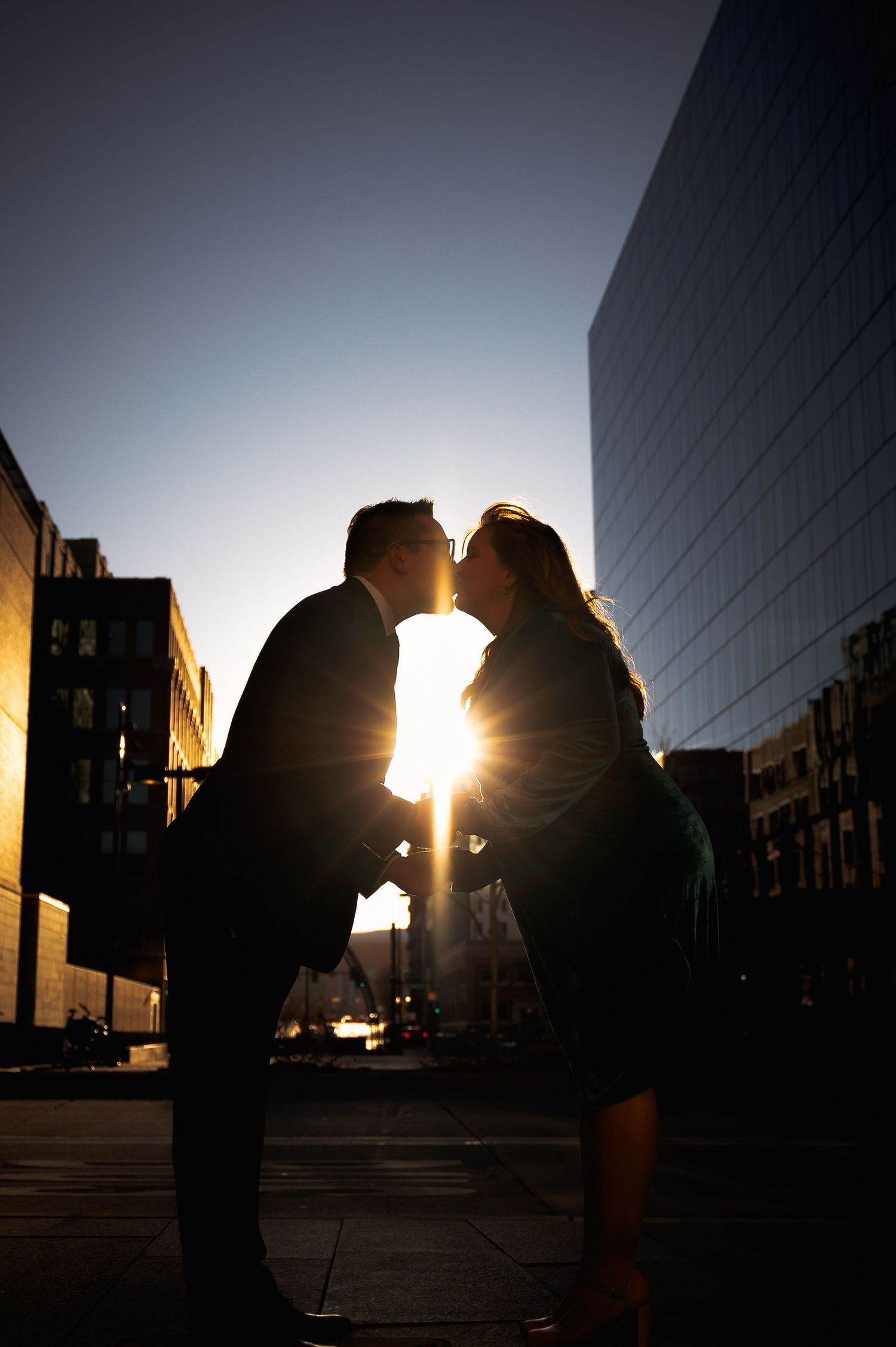 Romantic silhouette of a couple kissing against a golden sunset in an urban cityscape.