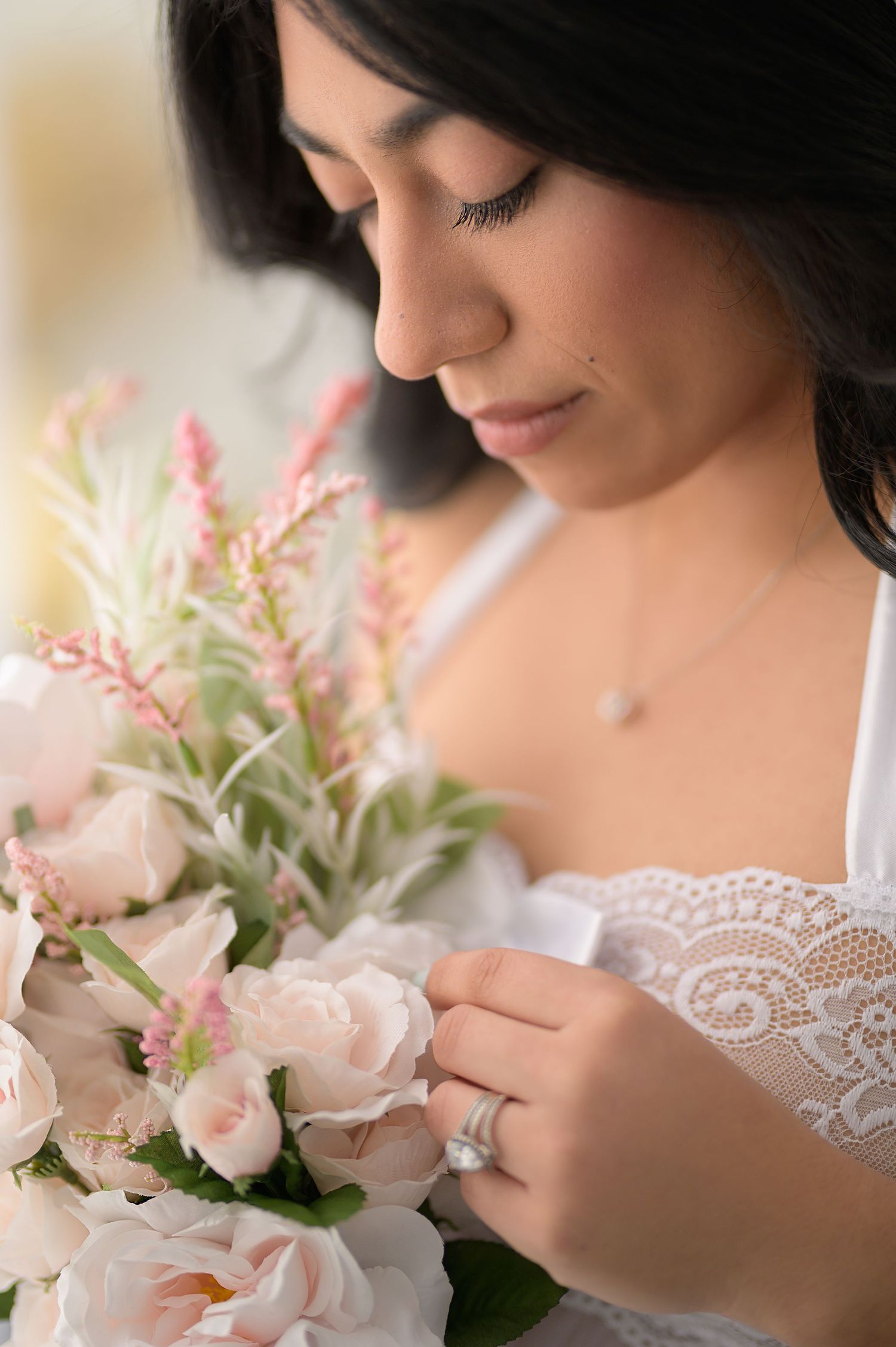 Close-up of bride admiring pink rose bouquet wearing lace dress and diamond ring.