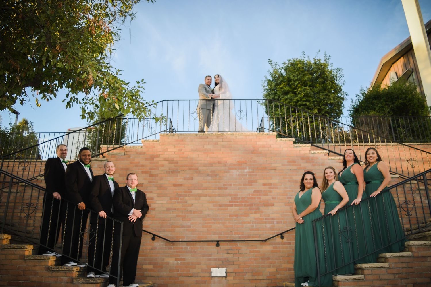 Wedding party poses on brick staircase with bridesmaids in green dresses and groomsmen in black.