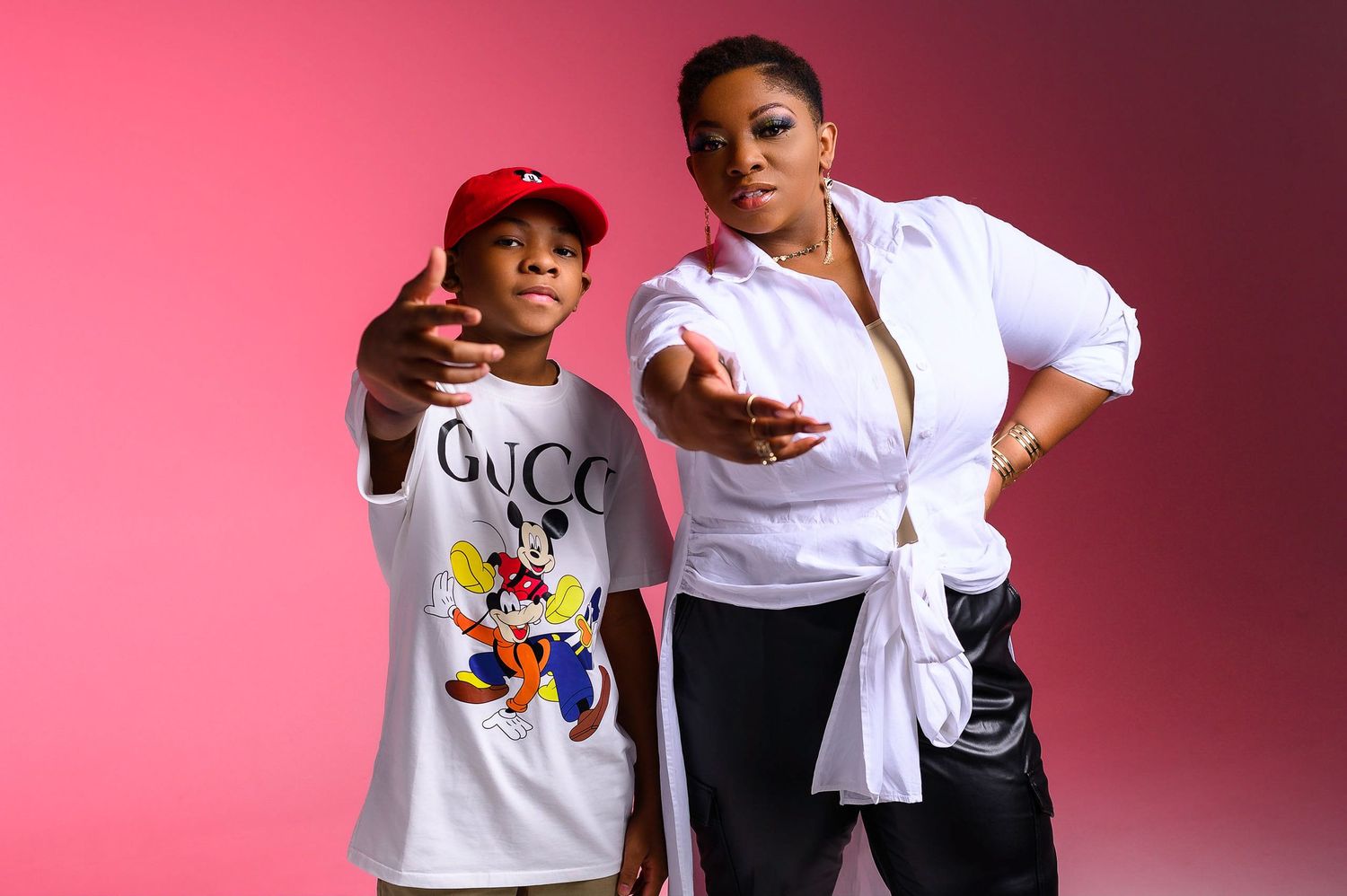 Mother and son posing together against a pink background in stylish outfits.
