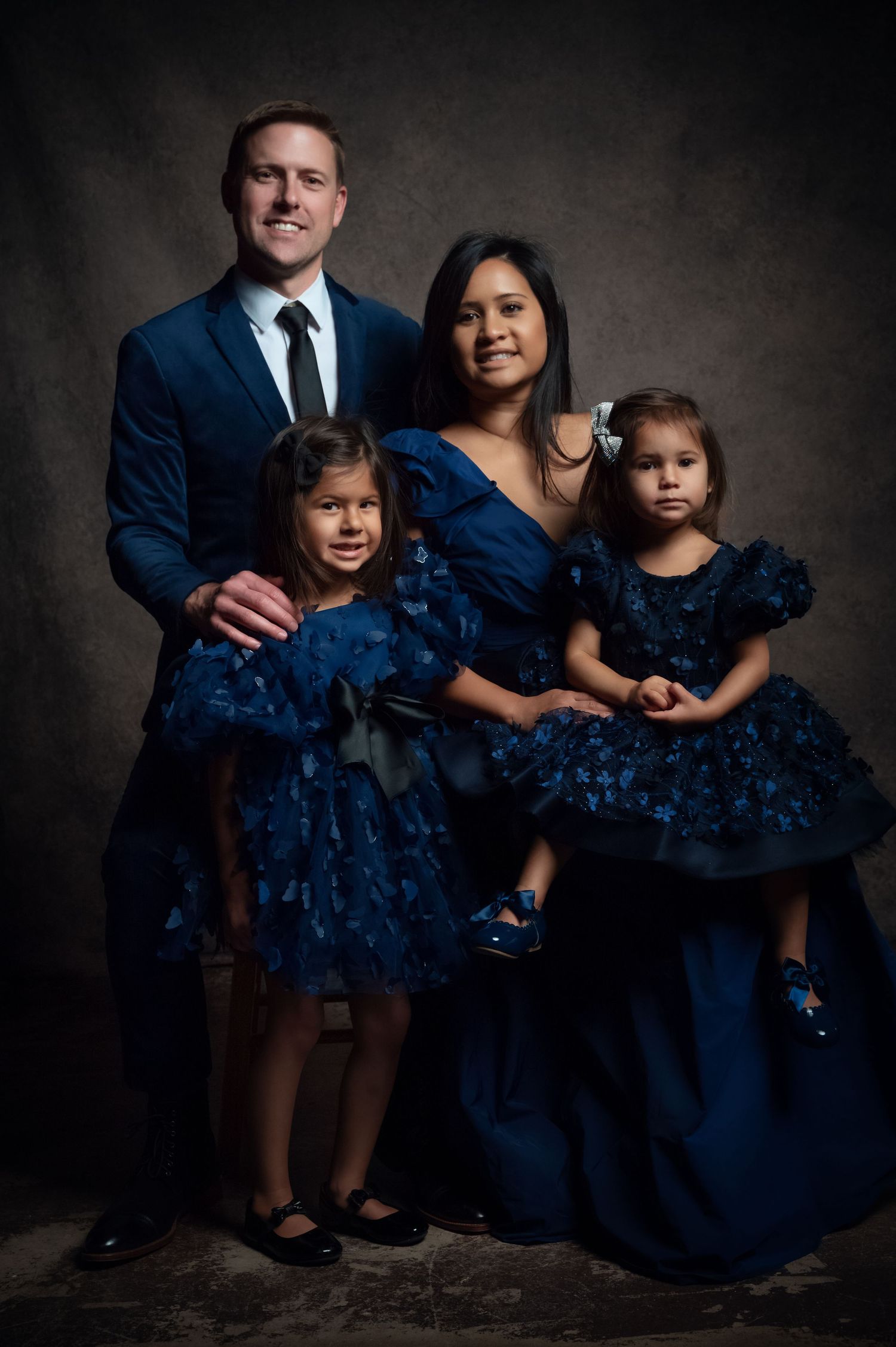 Family of four in matching navy blue formal outfits posing for elegant studio portrait photography.