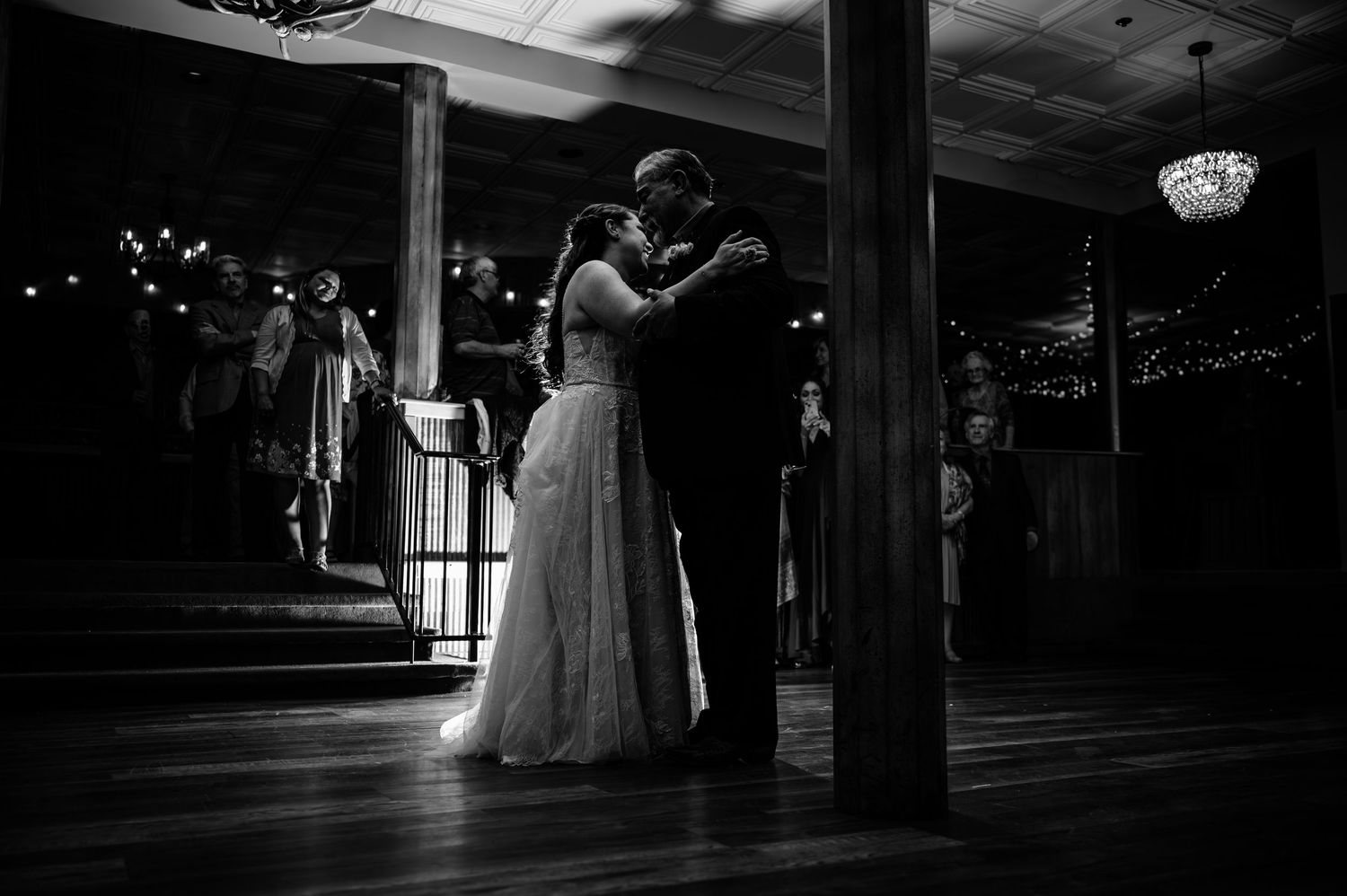 Black and white photo of bride and groom sharing first dance in dimly lit elegant wedding venue.