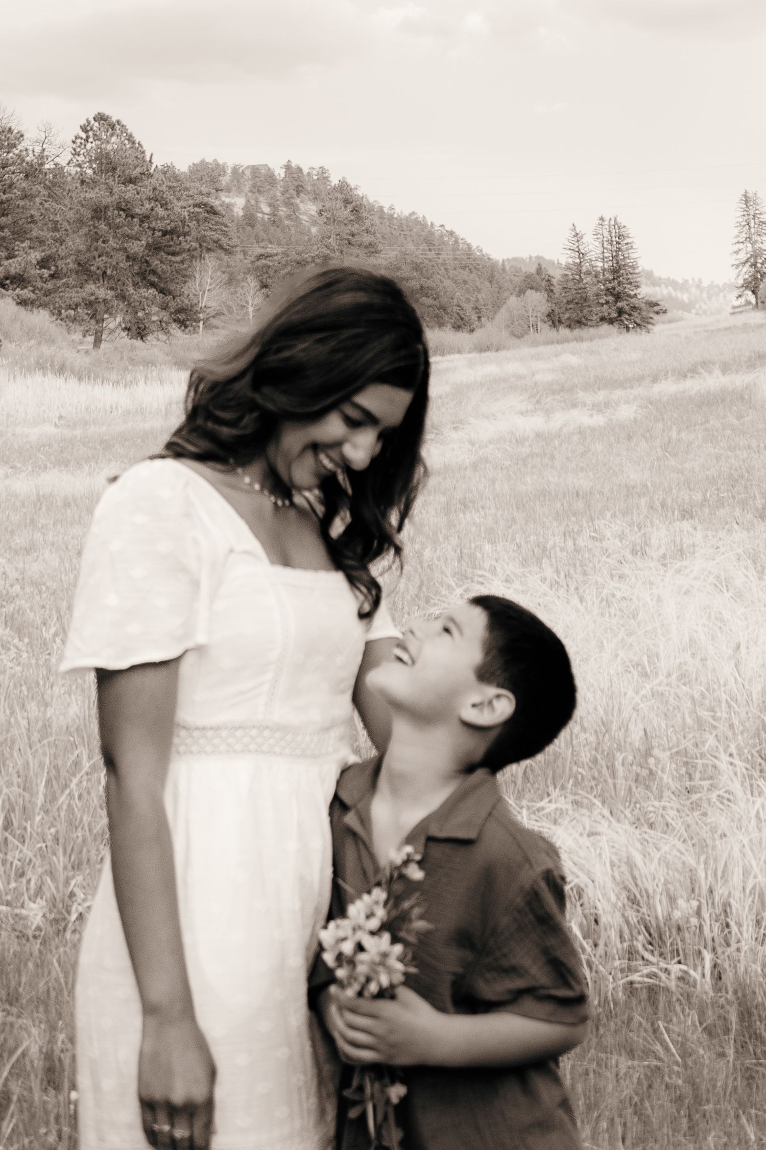 Black and white photo of mother and son smiling at each other in a meadow.
