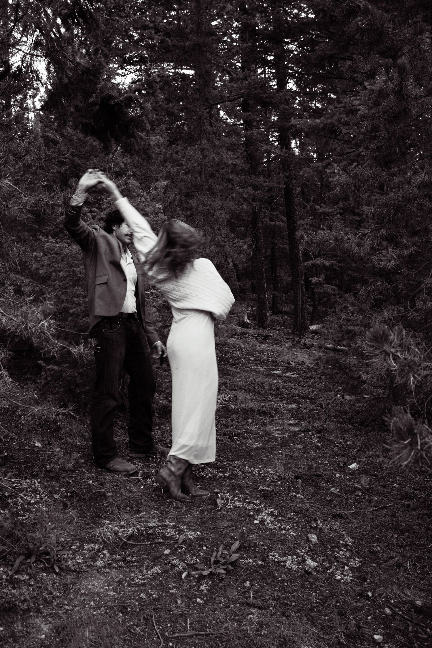 A couple dances romantically on a forest path in a black and white photo, woman in a white dress.