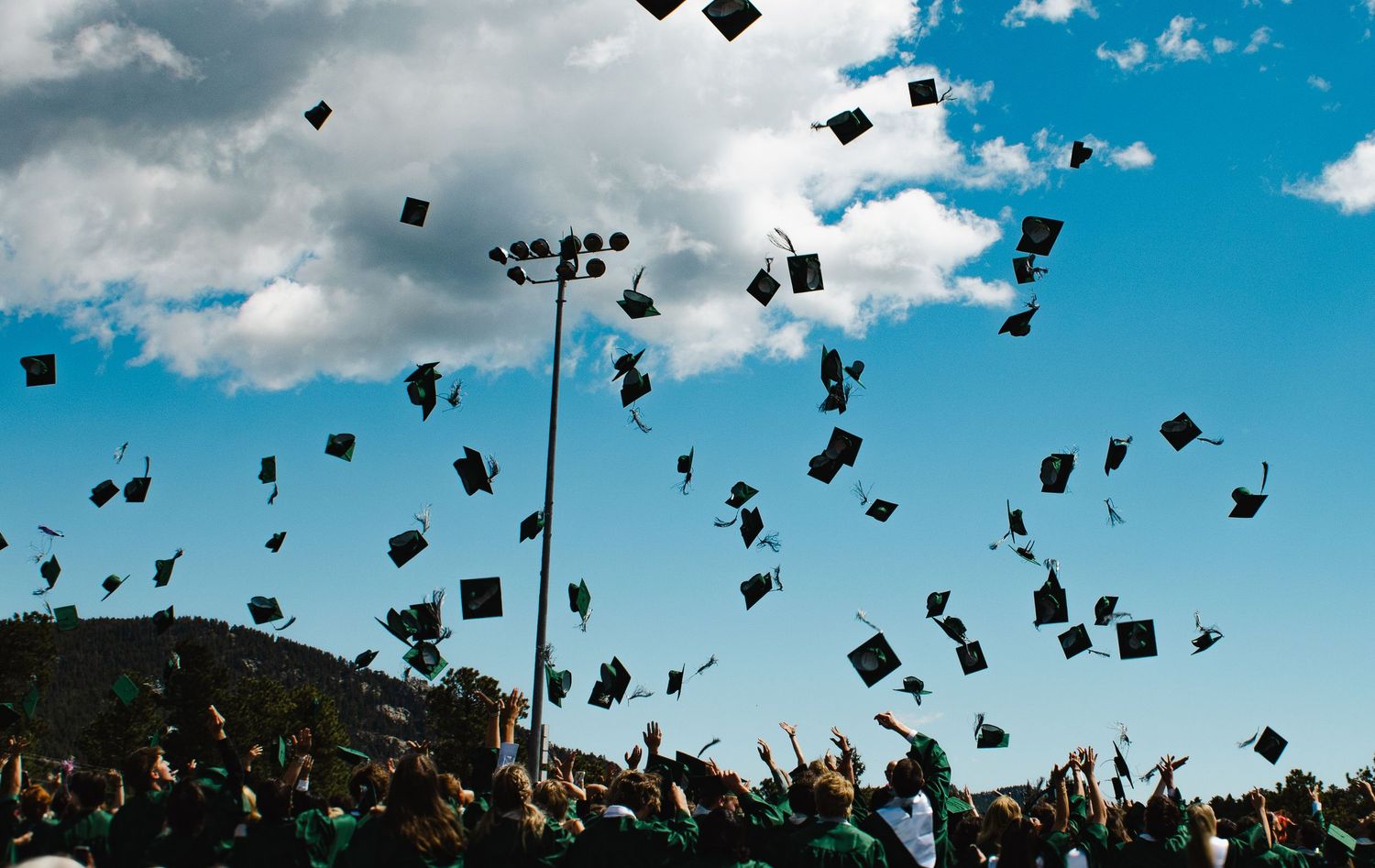 Graduation caps thrown into blue sky by celebrating graduates at outdoor ceremony.