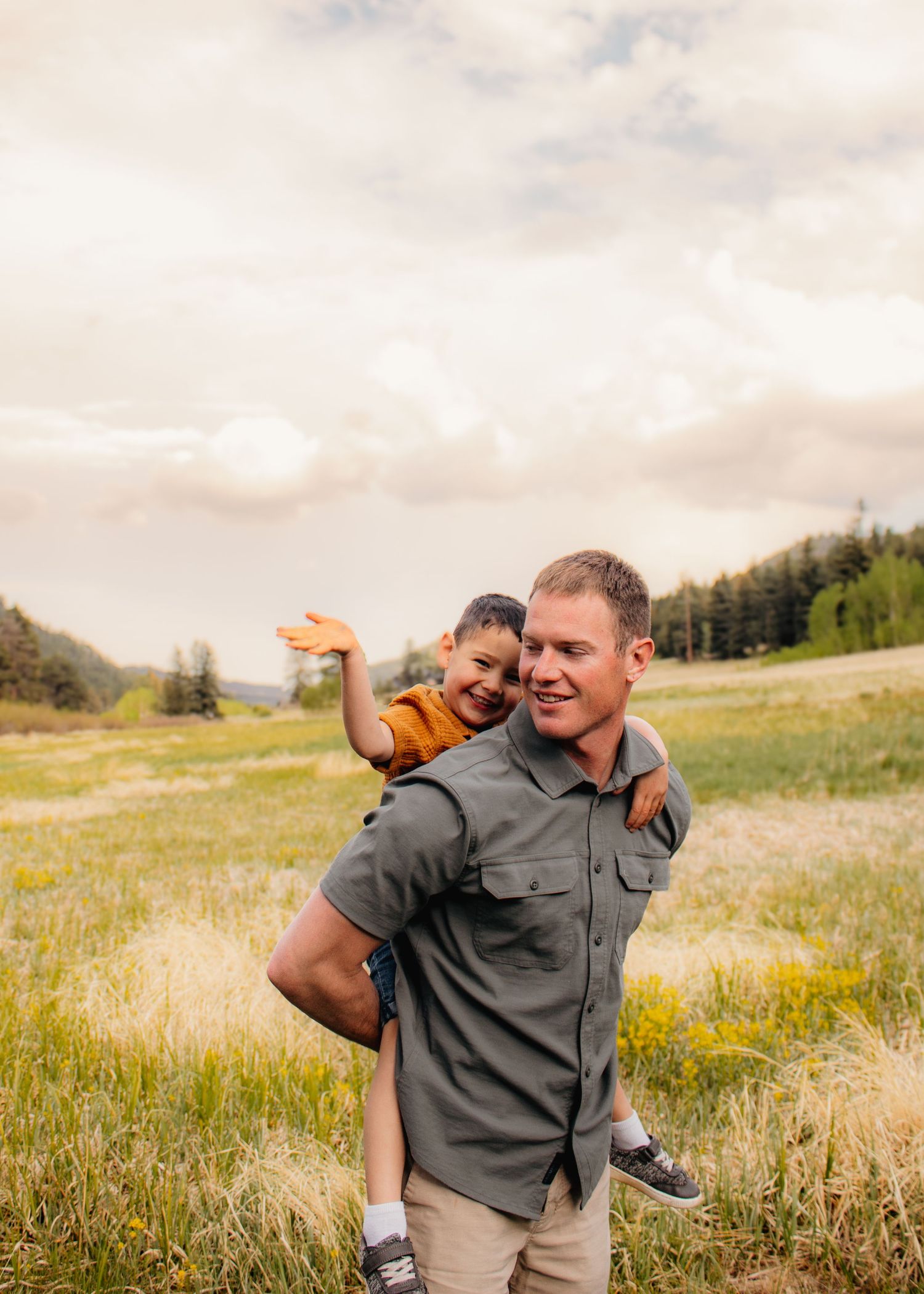 Father giving young son a piggyback ride in a sunny green mountain meadow.