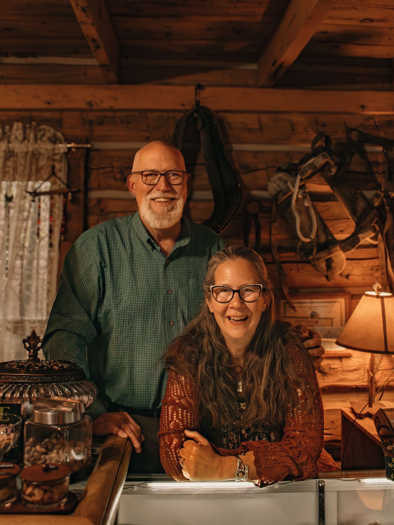 Smiling couple posing together inside a cozy rustic log cabin shop with warm lighting.