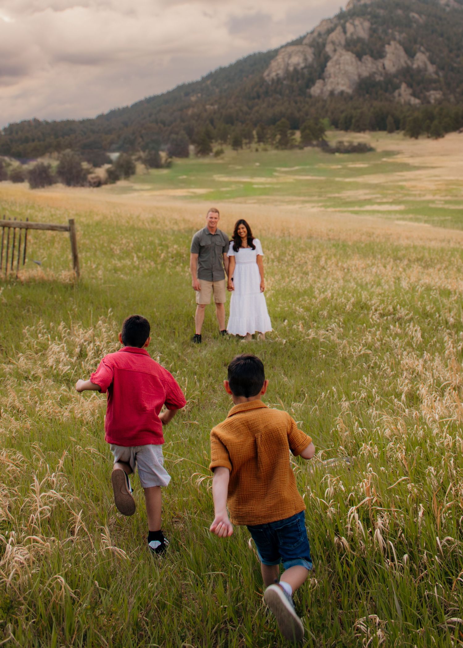 Two boys running toward their parents standing in a vast mountain meadow at dusk.
