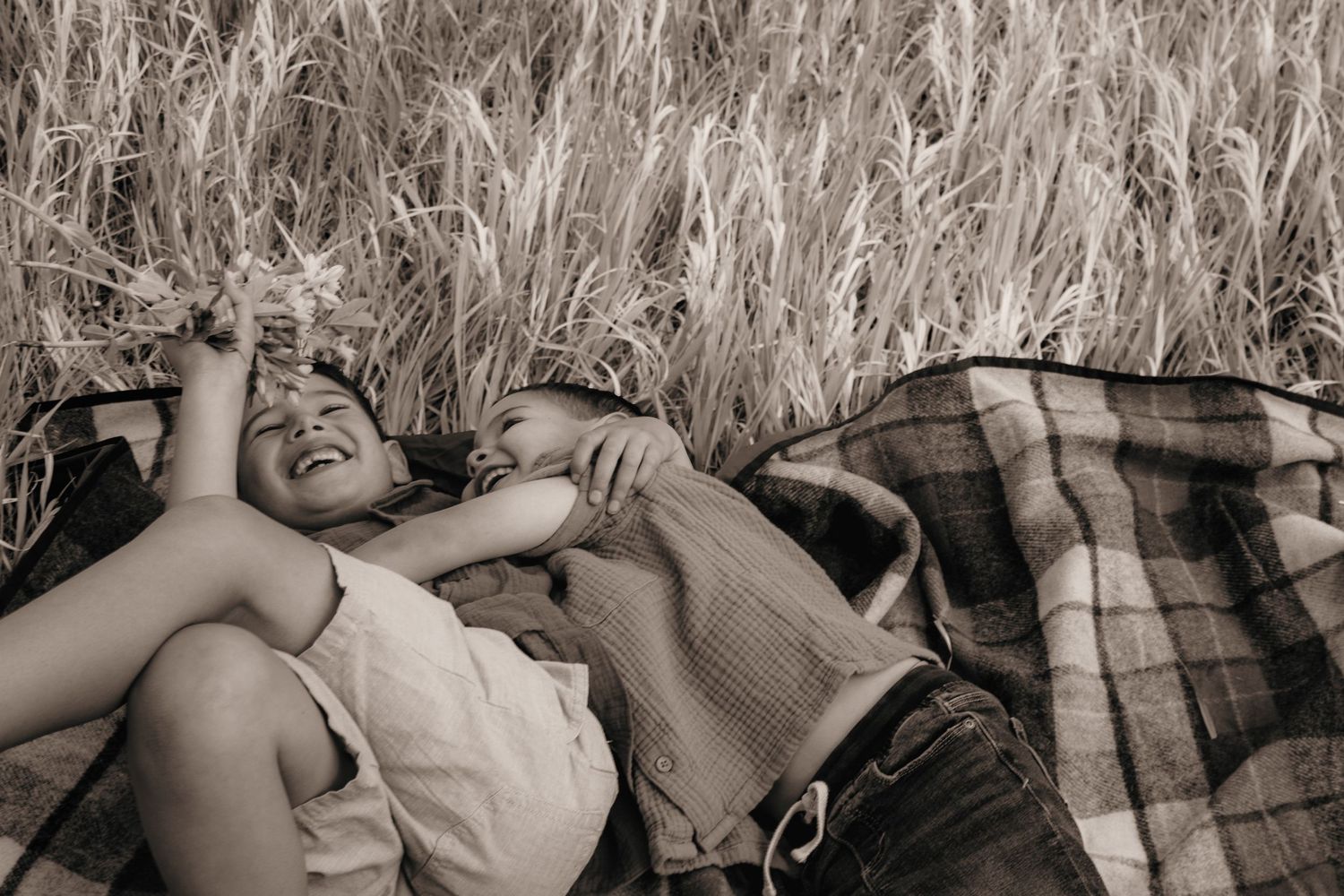 A child laughs joyfully while lying on a blanket in a wheat field in a sepia-toned photo.